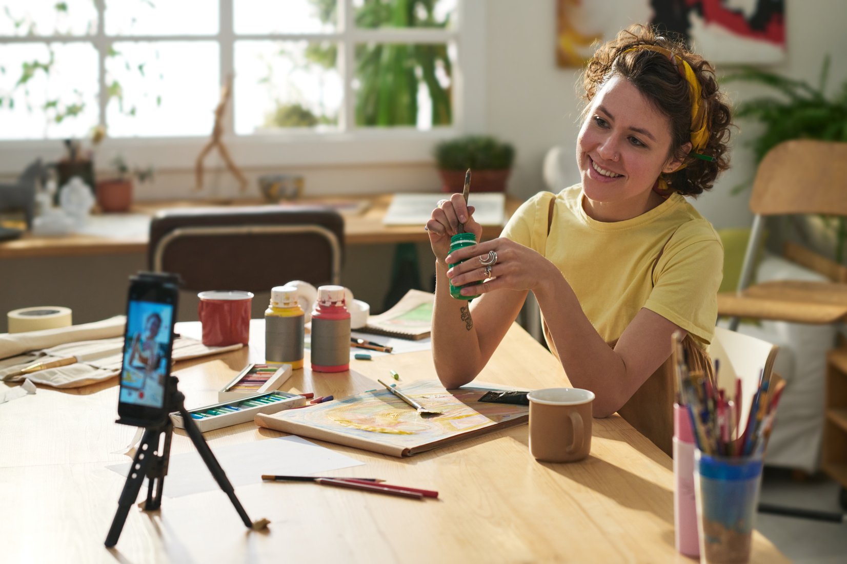 Young smiling creative woman with paintbrush and gouache during masterclass