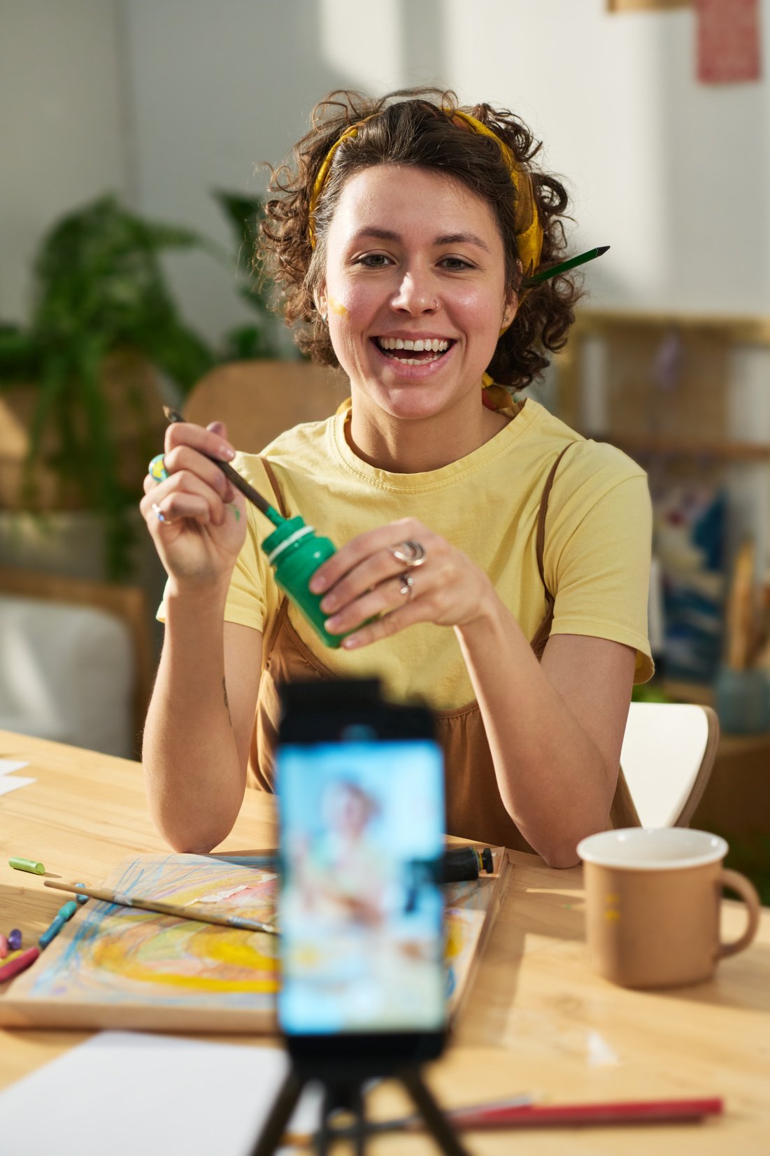 Young cheerful woman painting in front of smartphone during masterclass